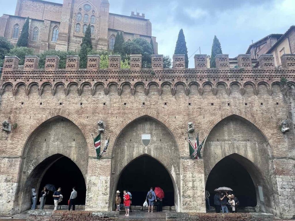 Fontebranda Brunnen in Siena mit Steinnbögen im Vordergrund, in denen Menschen stehen