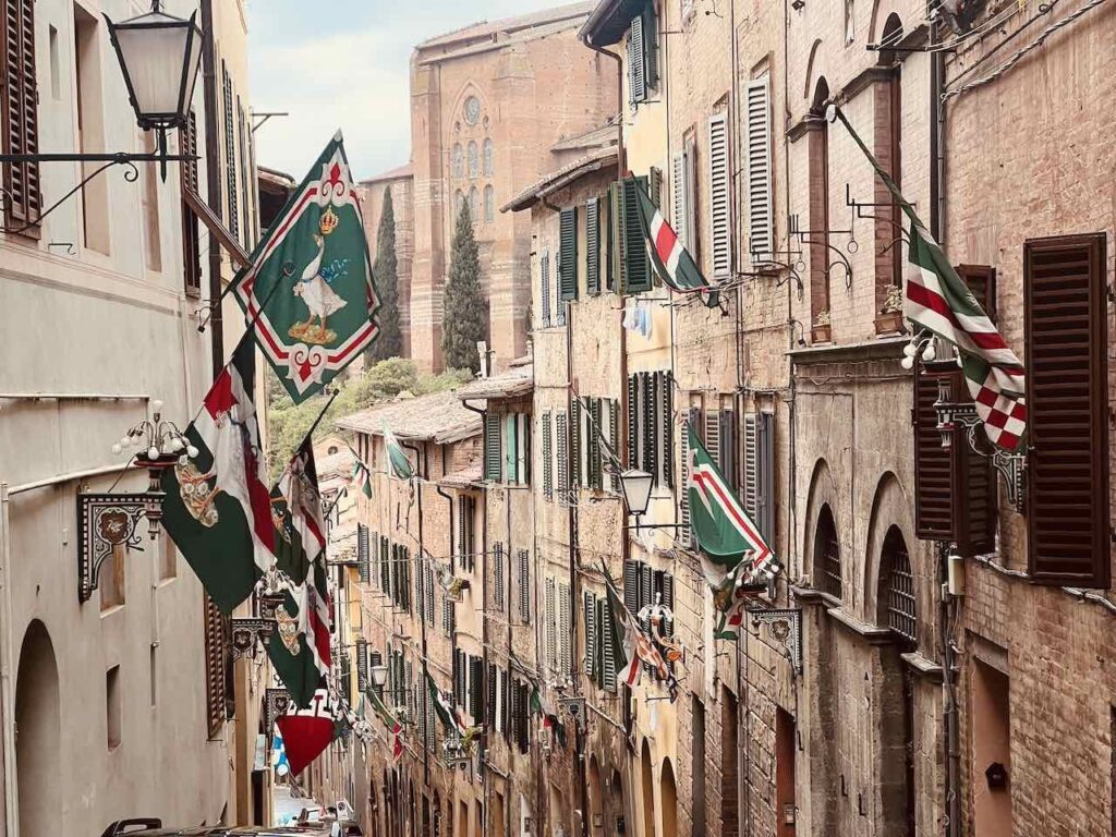 Altstadtgasse in Siena mit Fahnen, die aus den Fenstern hängen