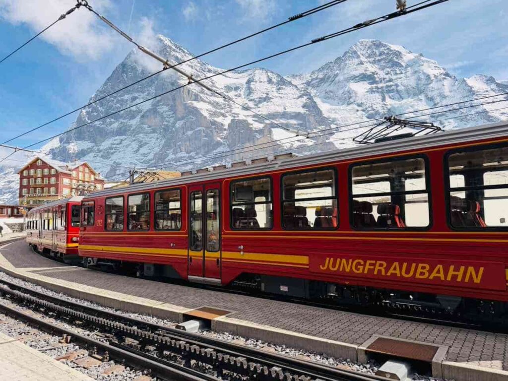 Die rote Jungfraubahn steht im Bahnhof Kleine Scheidegg in der Schweiz. Traumhaftes Panorama mit Bergspitzen hinter der Bahn.