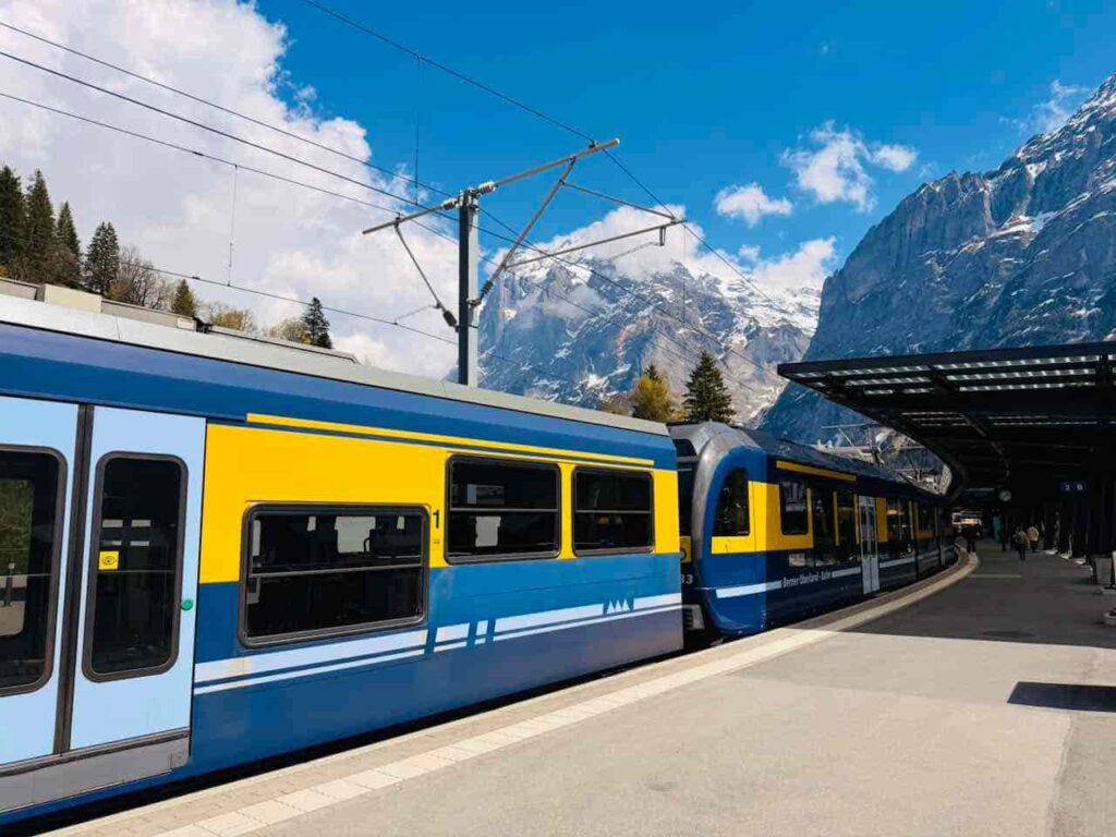 Zug in einem Schweizer Bahnhof stehend. Im Hintergrund eine schneebedeckte Bergkulisse.