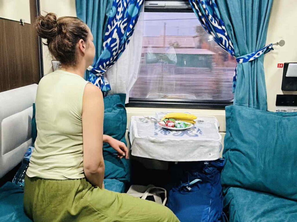 Auf dem Bett sitzend im Nachtzug in Usbekistan und aus dem Fenster blickend.
